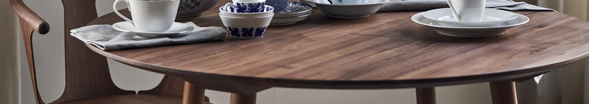A wooden dining table set with white cups, plates, and patterned blue and white bowls.