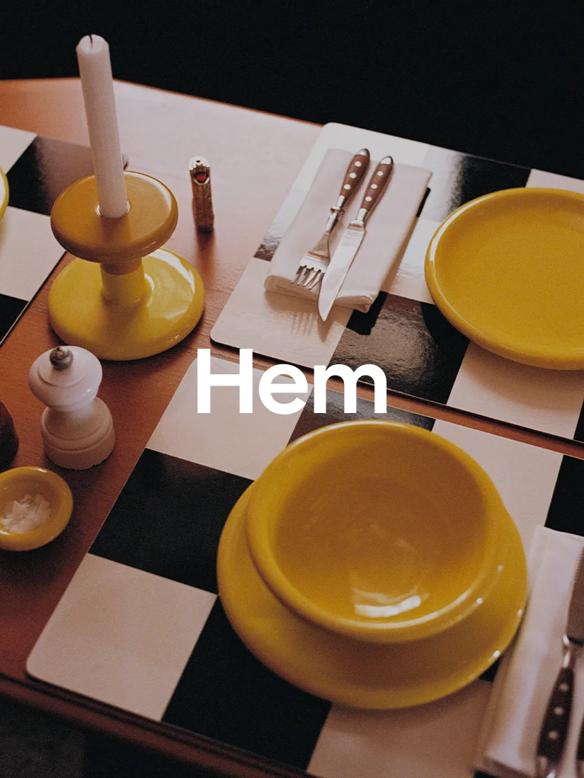 Table set with yellow plates, yellow candle holder, silverware, and salt shaker on a checkered placemat. Text 'Hem'.