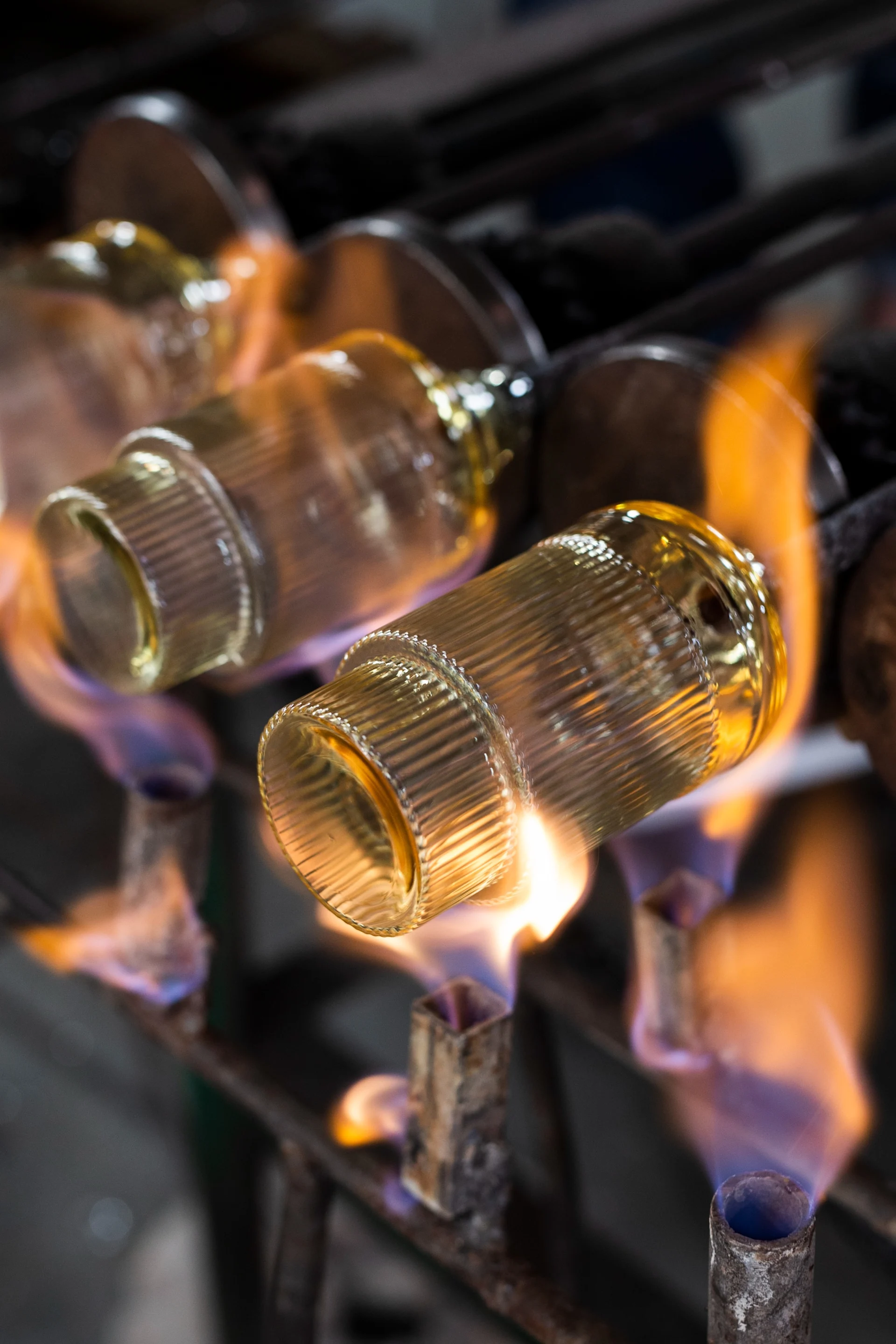 Ribbed cylindrical glass objects being heated by flames in a workshop.
