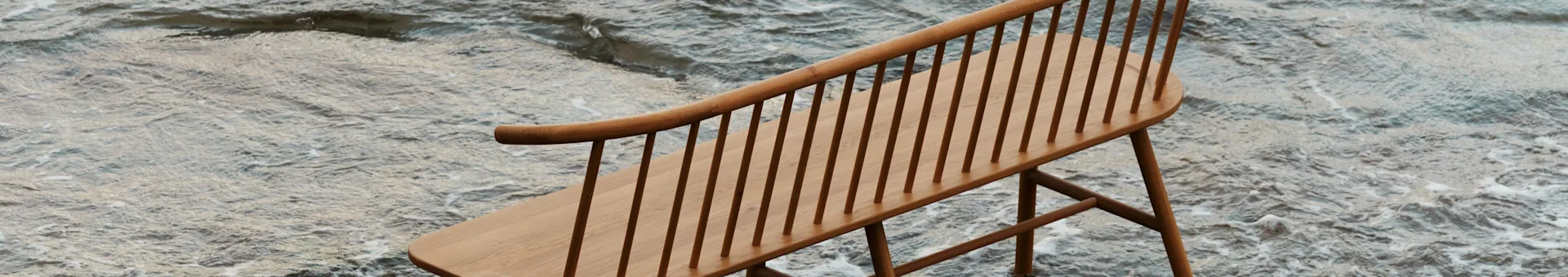 A light wooden spindle-back bench with a curved backrest, partially submerged in shallow, rippling water.