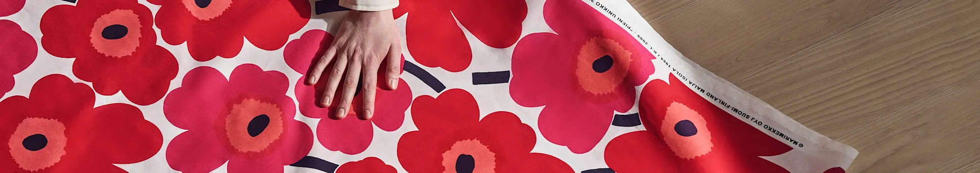 Hand resting on a fabric with a large red and pink floral pattern, on a wooden surface.