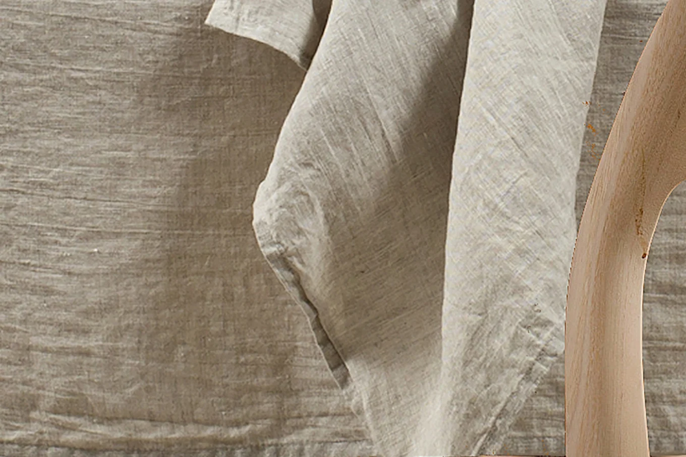 Close-up of a light brown linen fabric draped, with a curved wooden object on the right.