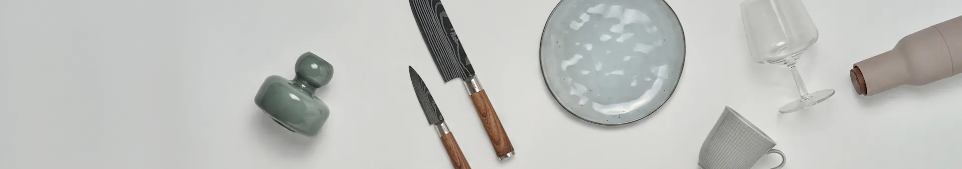 Various kitchen and dining items including a green vase, two knives, a speckled plate, a wine glass, a beige bottle, and a patterned mug.