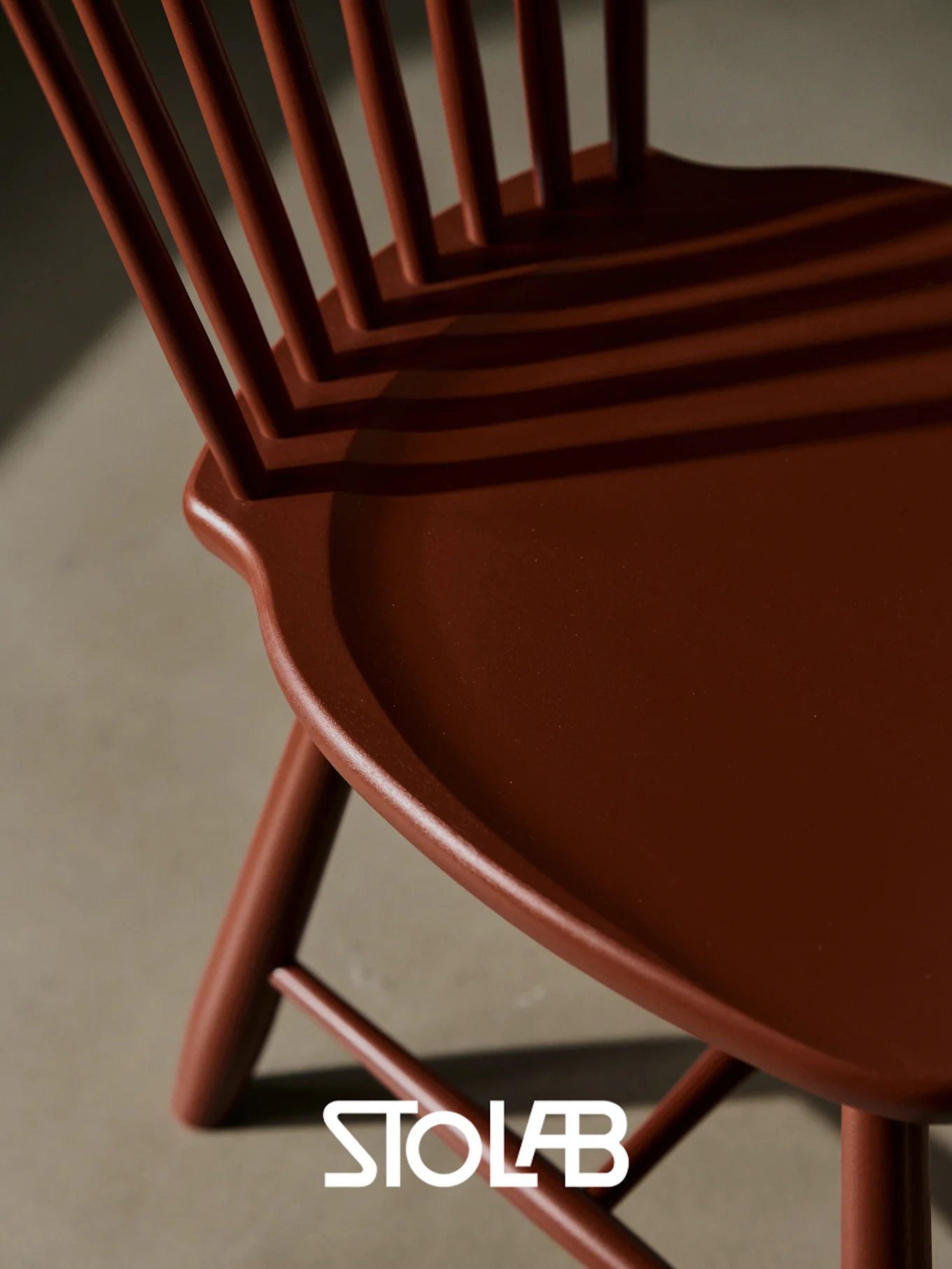 A reddish-brown wooden chair with a slatted back and contoured seat, casting shadows.
