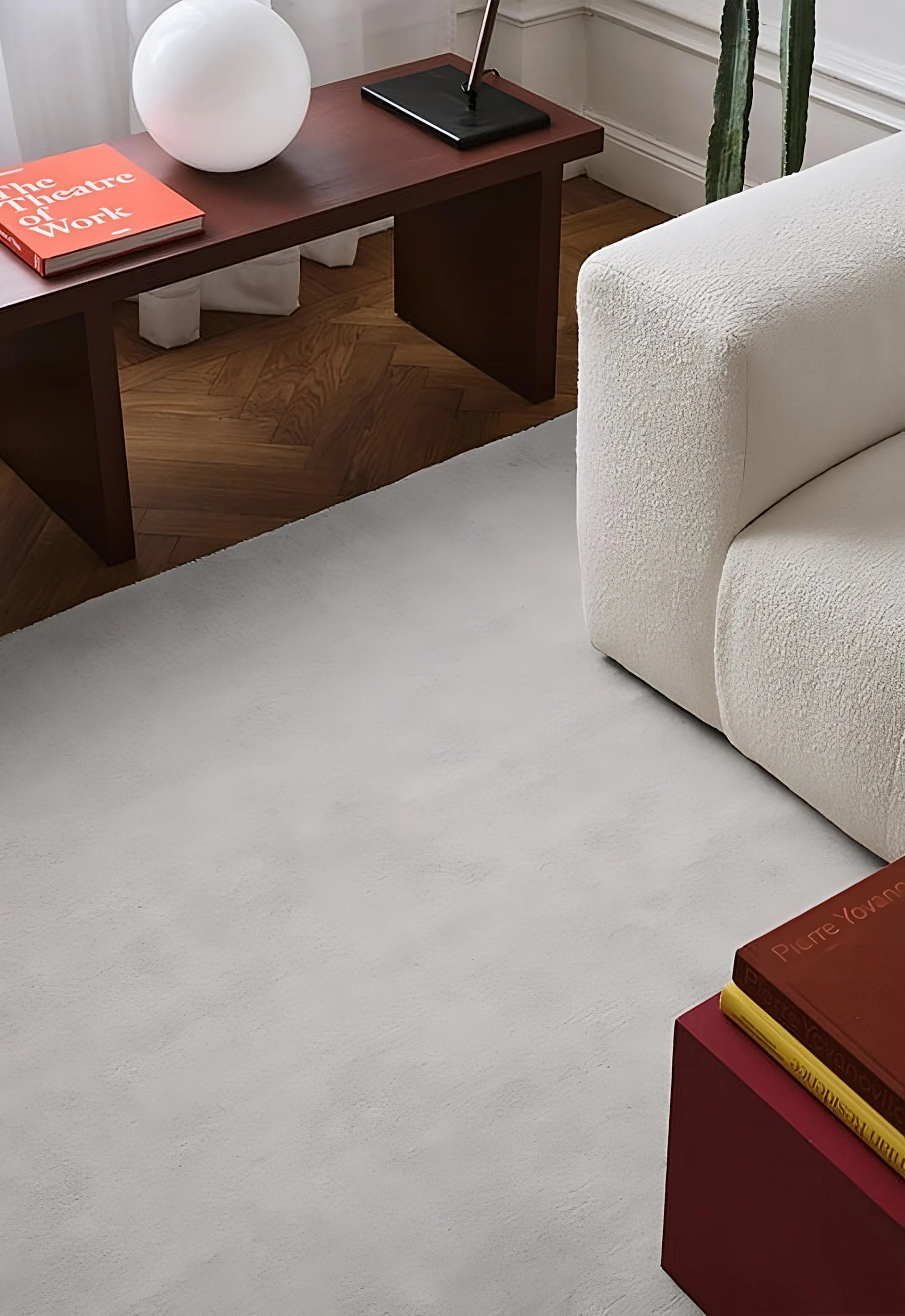 A living room featuring a light grey rug, a cream textured sofa, and a dark brown side table with a white spherical lamp and books.