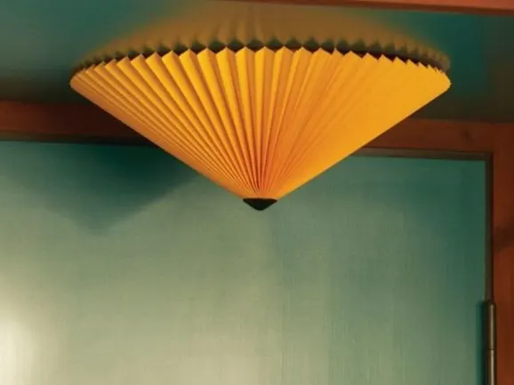 Yellow pleated conical ceiling fixture against a teal wall.