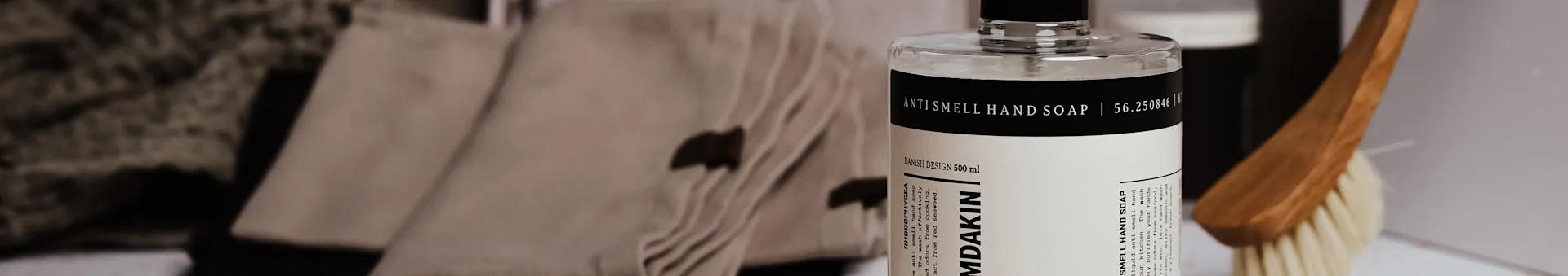 Damdakin Anti Smell hand soap bottle, 500ml, with folded brown towels and a brush.