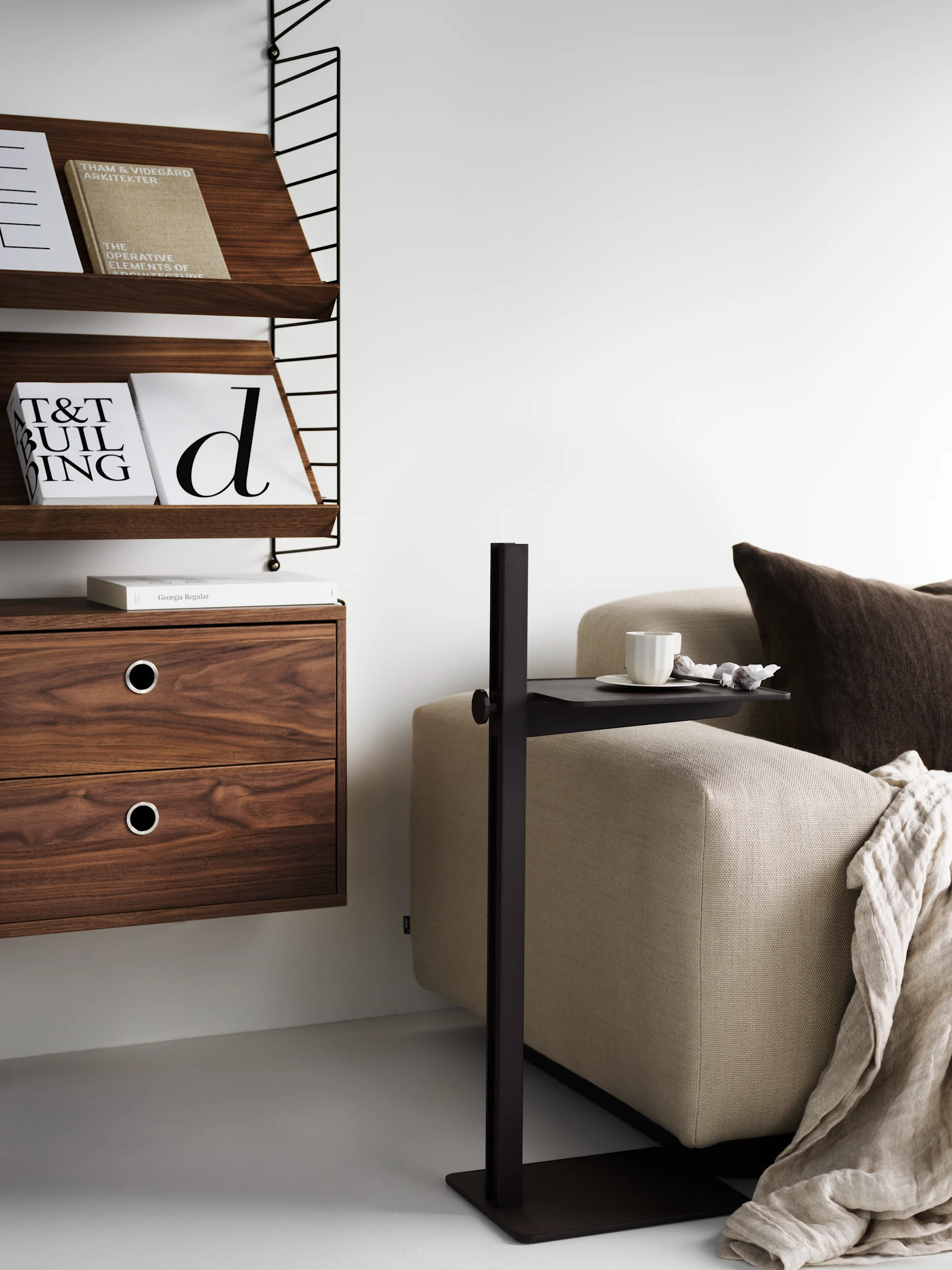 Modern living space with a wooden wall shelf, beige sofa, and a slim dark side table with a cup and snacks.
