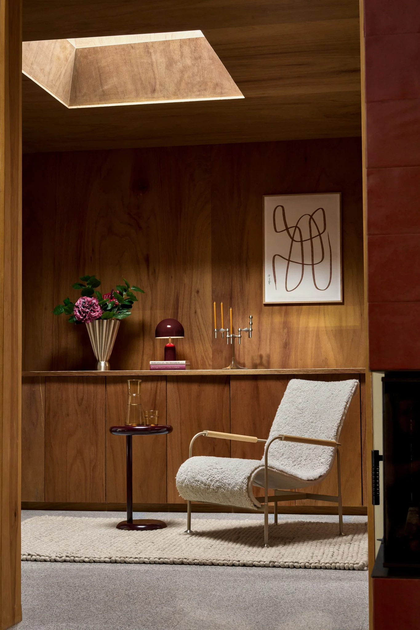 Cozy room with wood walls, cream bouclé armchair, side table, flowers, and abstract art.