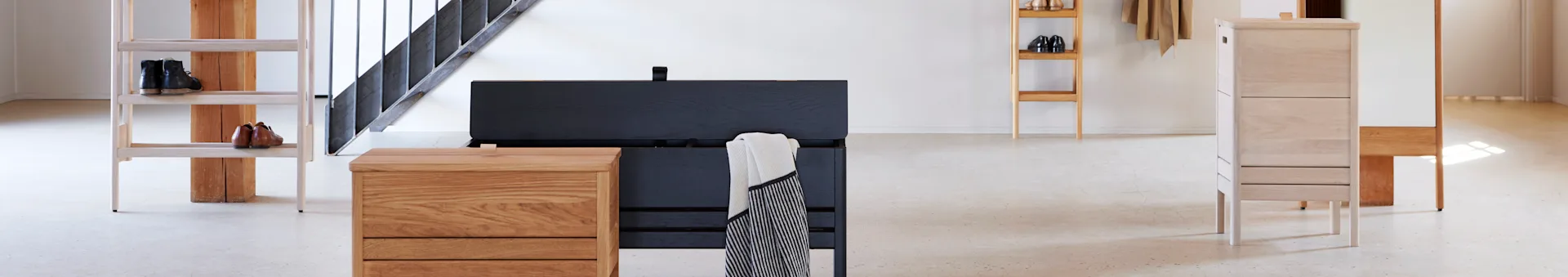 Modern entryway with light wood shoe rack holding boots, black and light wood chests, and a tall light wood cabinet.
