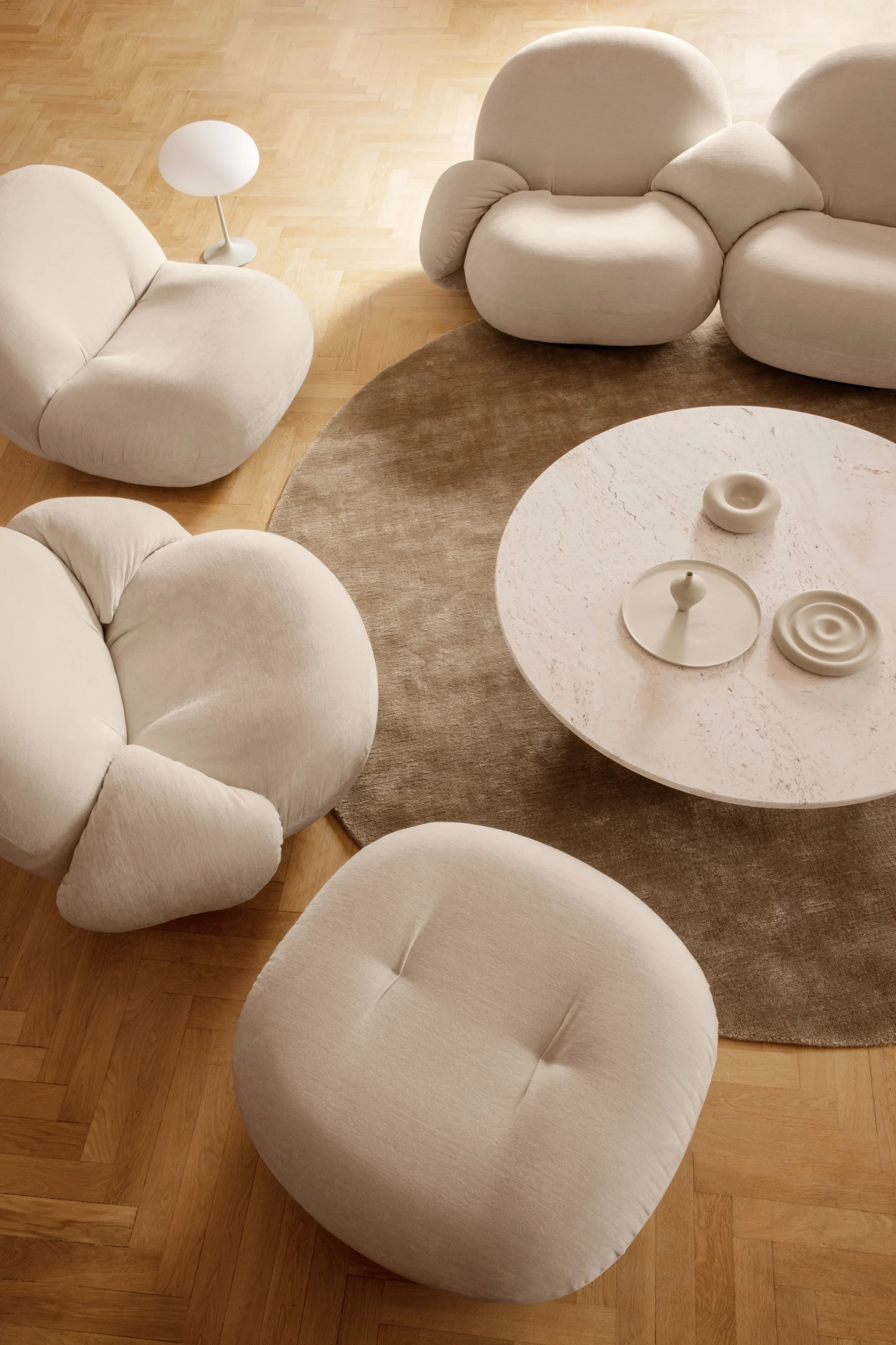 Overhead of a modern living room with soft, rounded beige sofas and chairs, a round marble coffee table, and a brown rug.