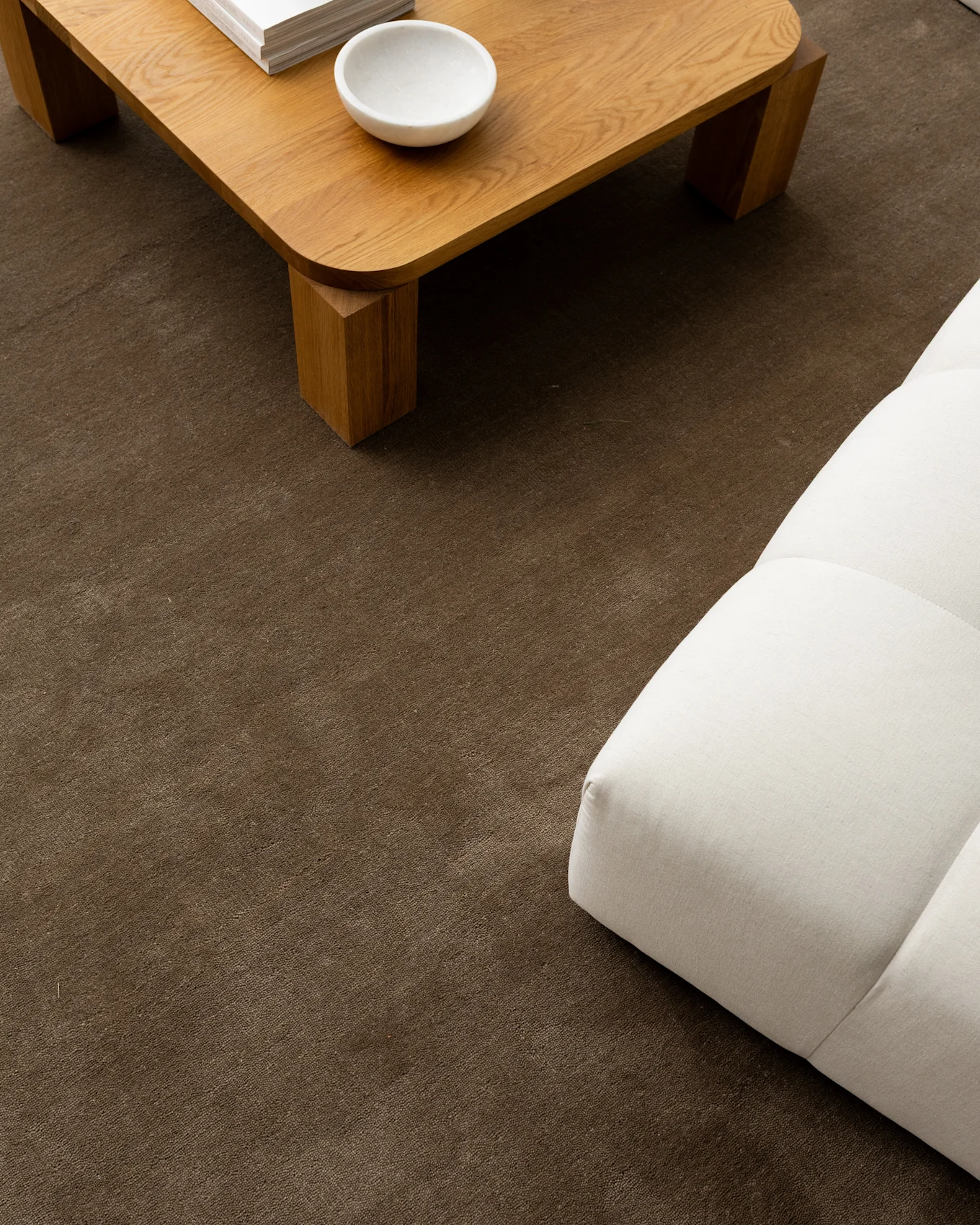 A light wooden coffee table with a white bowl and books, next to a white sofa on a brown textured rug.