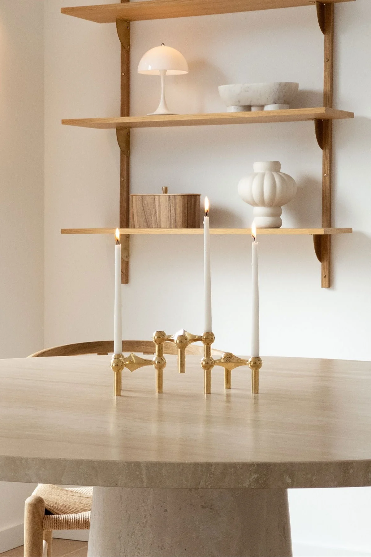 A golden candelabra with three lit candles on a round table, with shelves holding decorative objects behind.