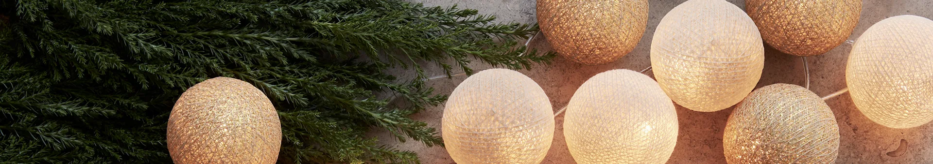 String of decorative lights with golden and white textured sphere covers, next to green foliage.