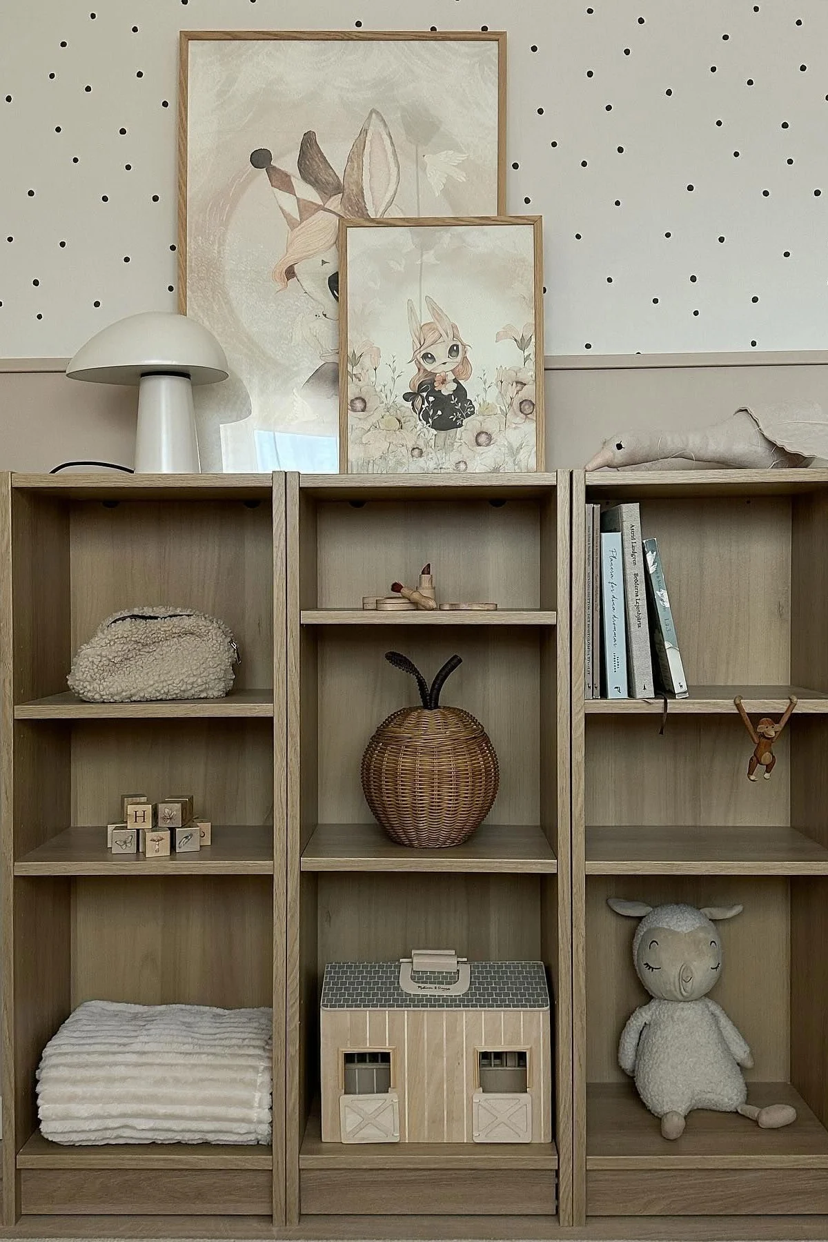 Three wooden bookshelves with children's toys and decor, including animal prints, a mushroom lamp, and a plush sheep.