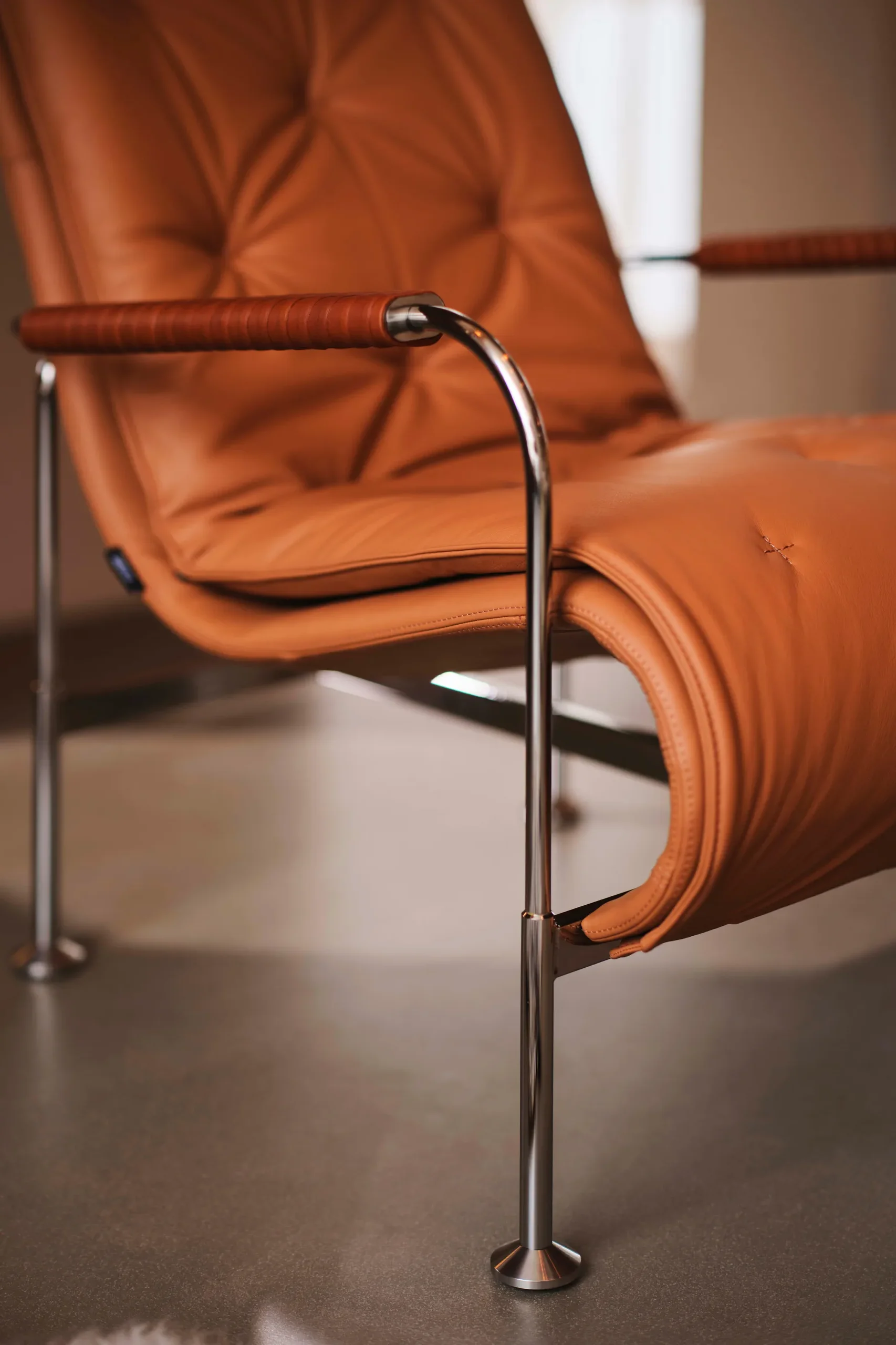 Tan leather armchair with chrome frame and wrapped armrests.
