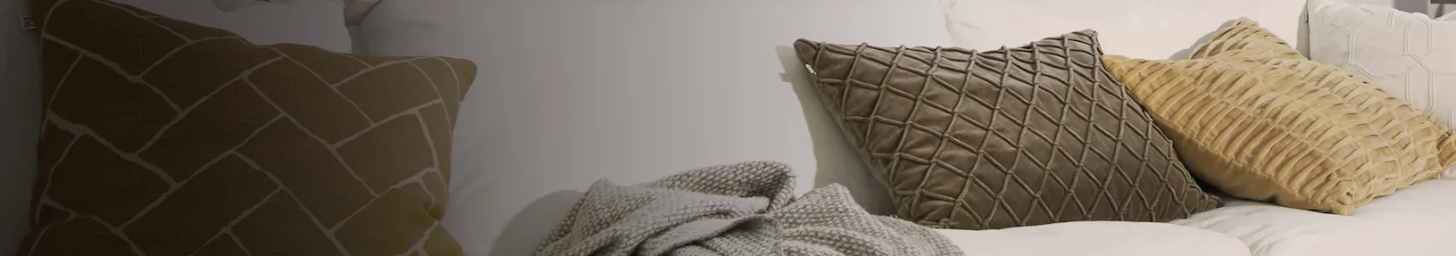 Assortment of throw pillows in brown, tan, gray, and white with various textures and patterns on a bed.