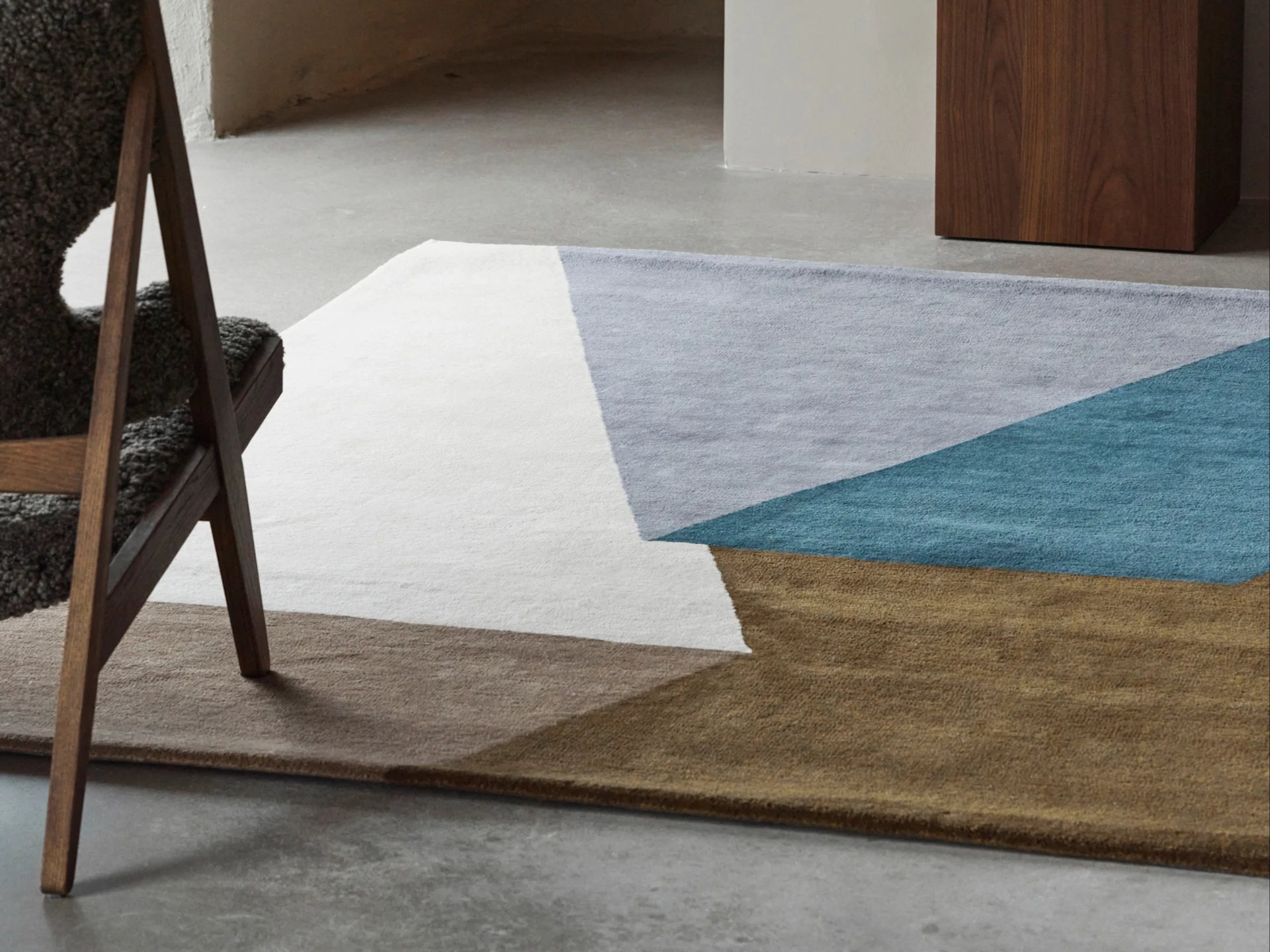 A geometric rug in white, light grey, teal, and brown, partially visible on a concrete floor next to a wooden chair.