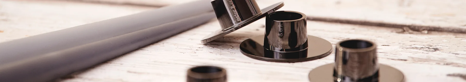 Several dark, cylindrical components, one tilted to show 'ester & erik', on a light wooden surface.