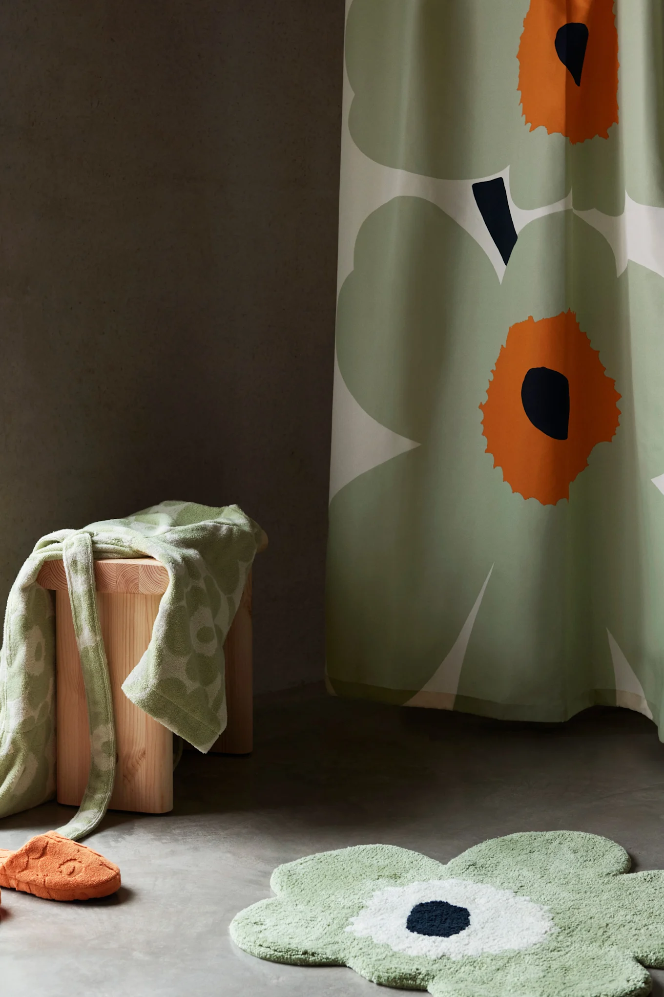 Bathroom decor with green floral shower curtain, bathmat, towel on stool, and orange slipper.