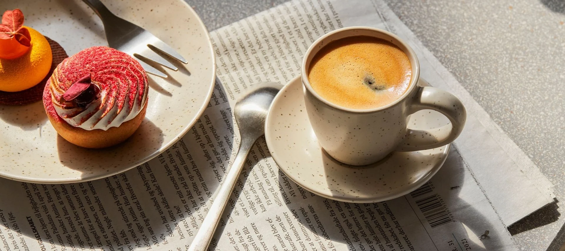 Coffee cup and two pastries, a red tart and an orange one, on a newspaper.