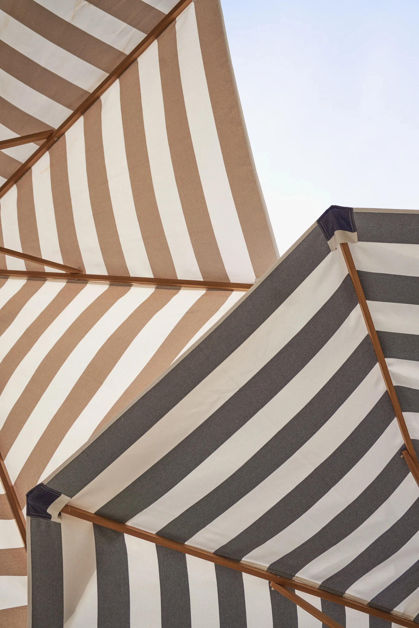 Two striped beach umbrellas against a blue sky, one brown and white, the other grey and white.