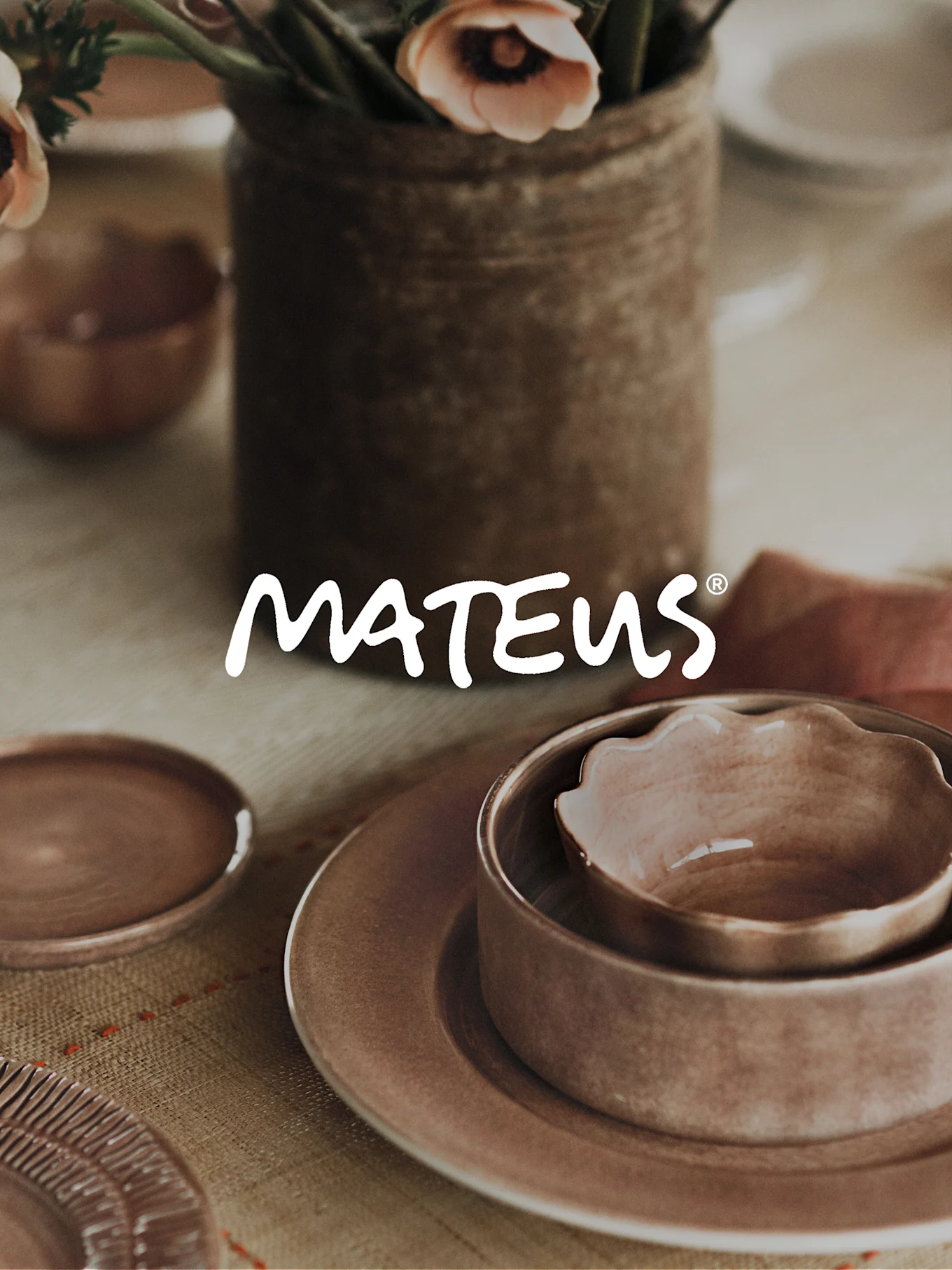 MATEUS® logo over an earthy ceramic table setting with plates, nested bowls, and a vase of pink flowers.