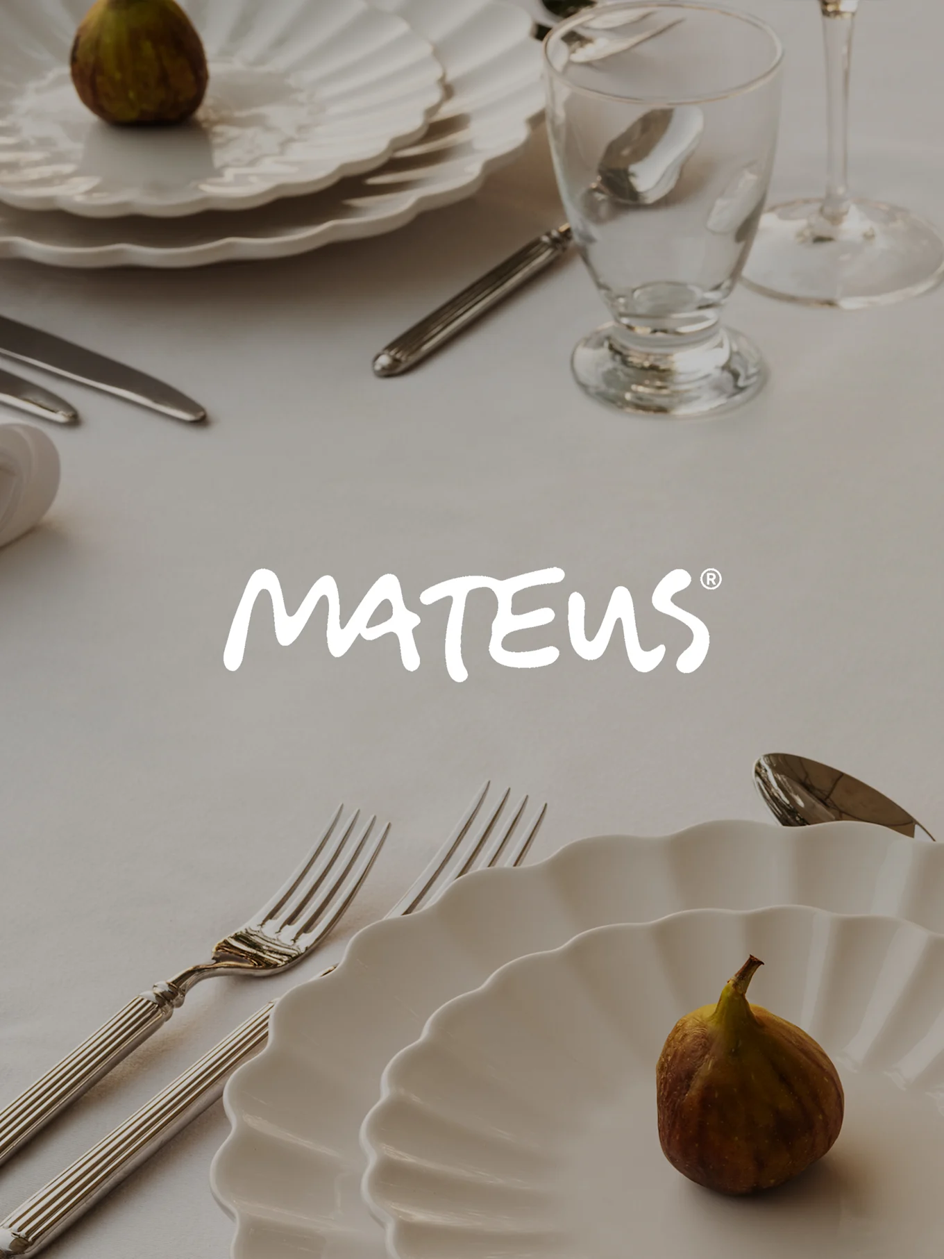 Table setting with white ruffled plates, silver cutlery, a clear glass, and figs, featuring the MATEUS logo.