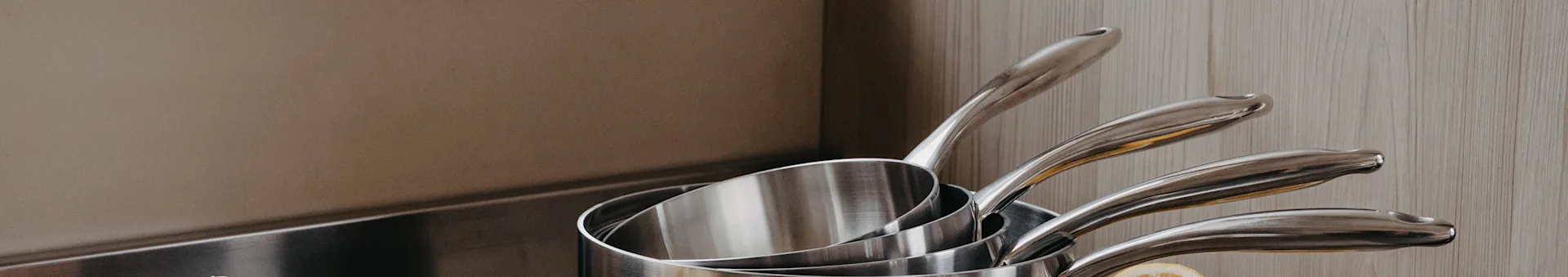 Stacked stainless steel saucepans on a counter with wood paneling in the background.