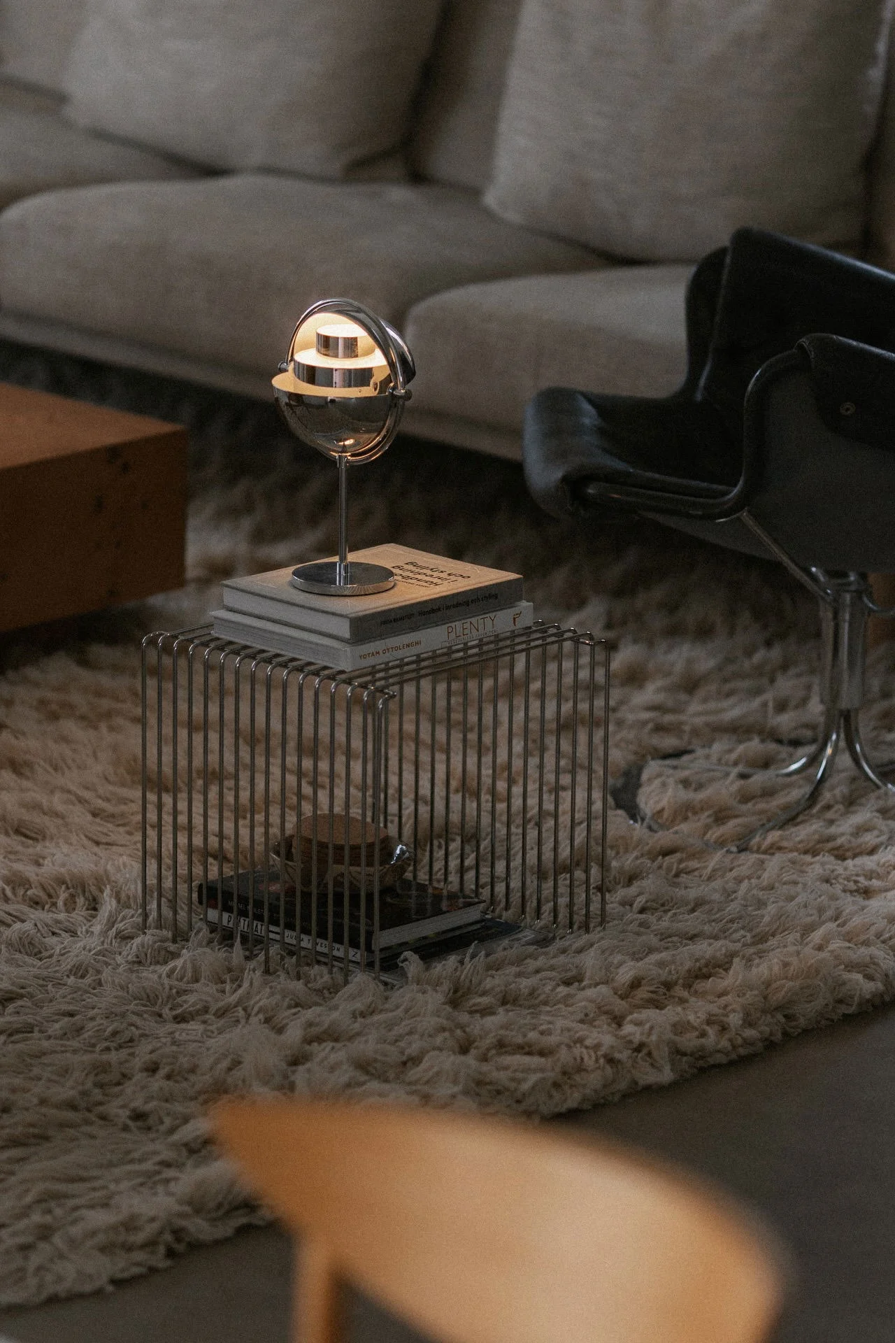 Modern living room with a chrome globe lamp on books atop a wired side table, set on a textured rug.