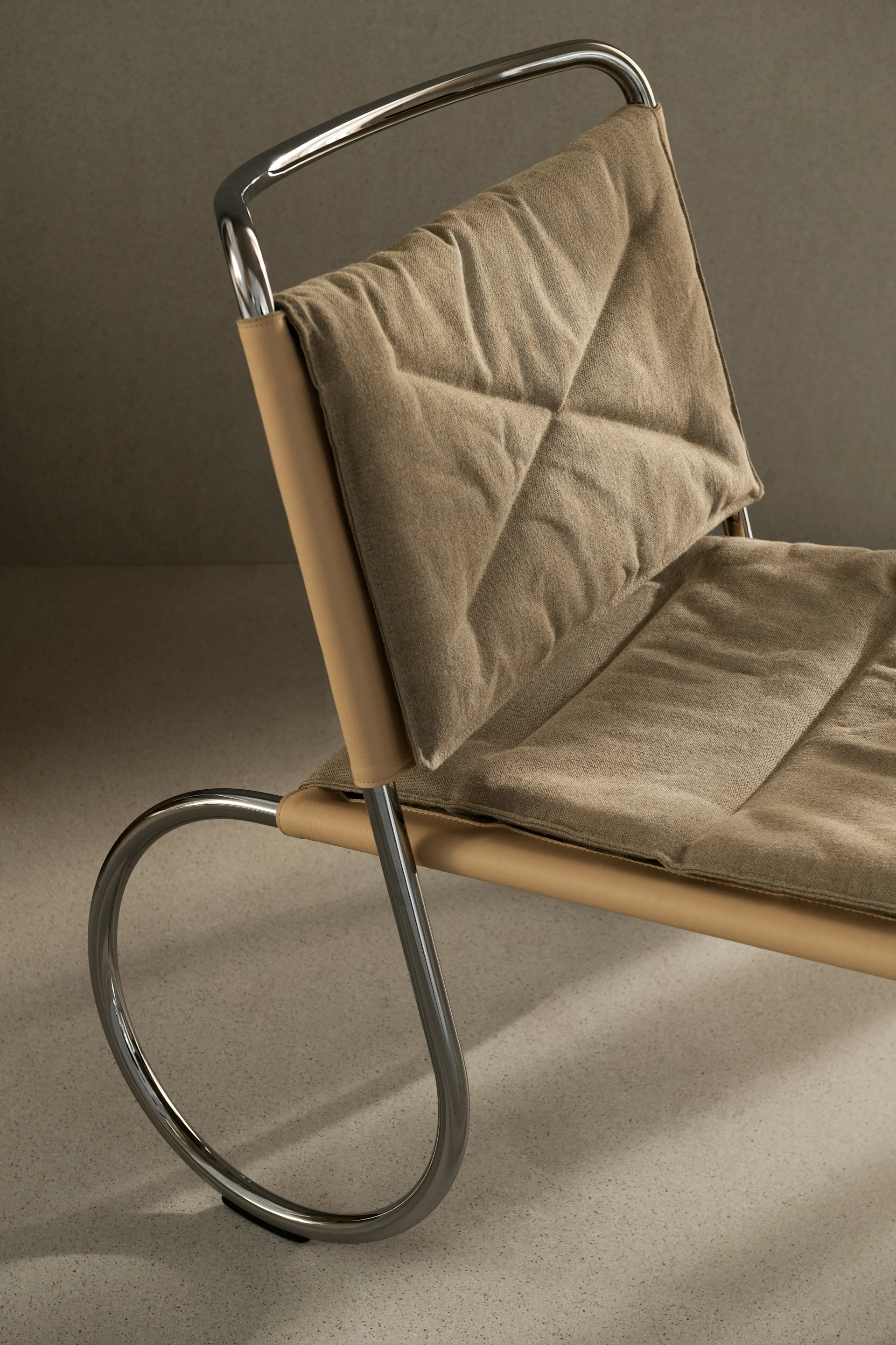 Close-up of a modern chair with a polished chrome frame, tan leather sling, and quilted beige fabric cushions.
