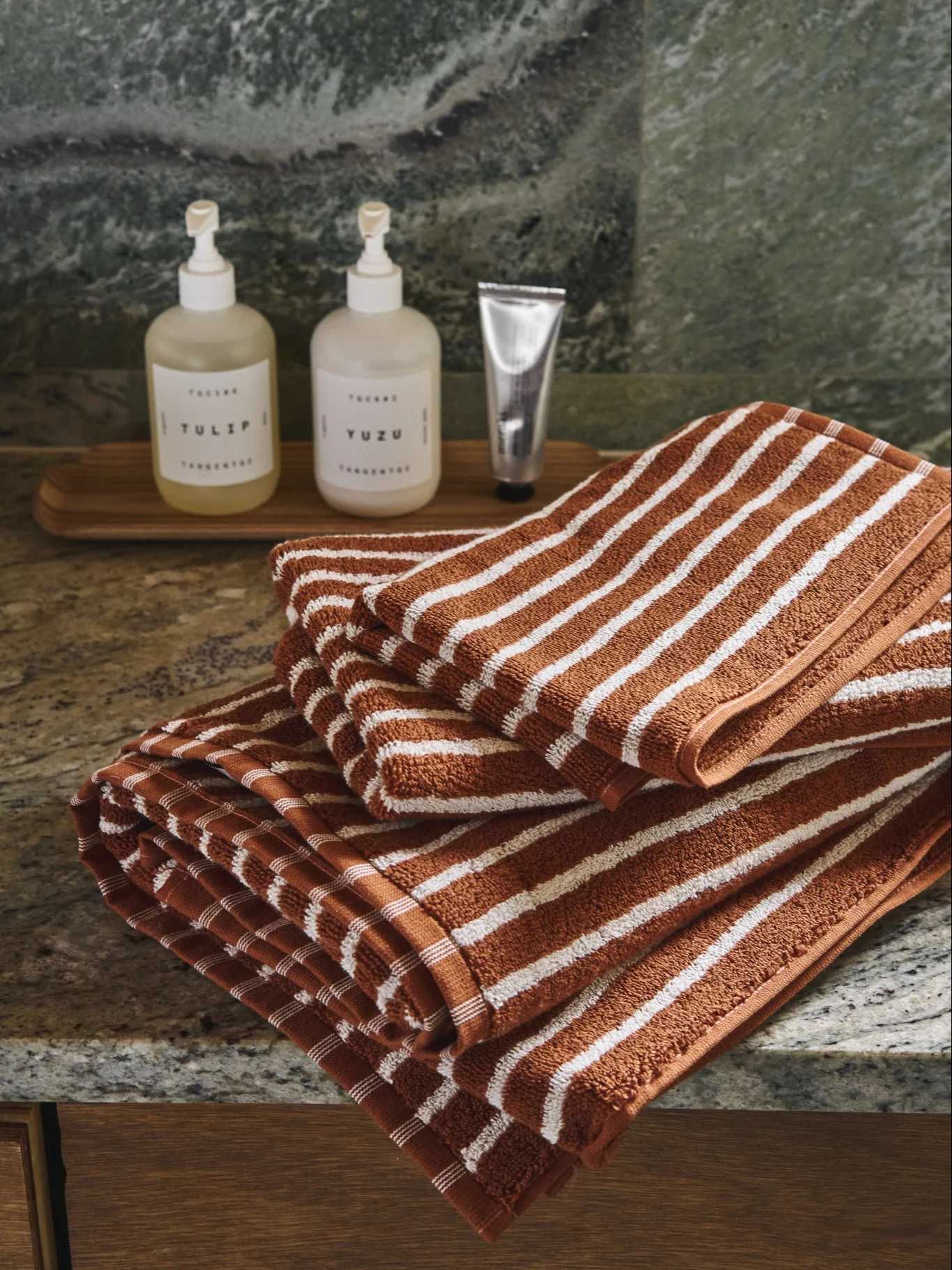 Stack of folded rust and white striped towels on a mottled countertop with soap dispensers behind.
