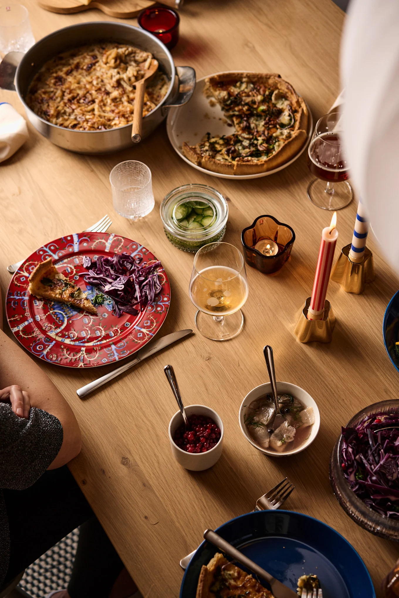A festive dinner table with a casserole, quiche, pickled herring, red cabbage, and lit candles.