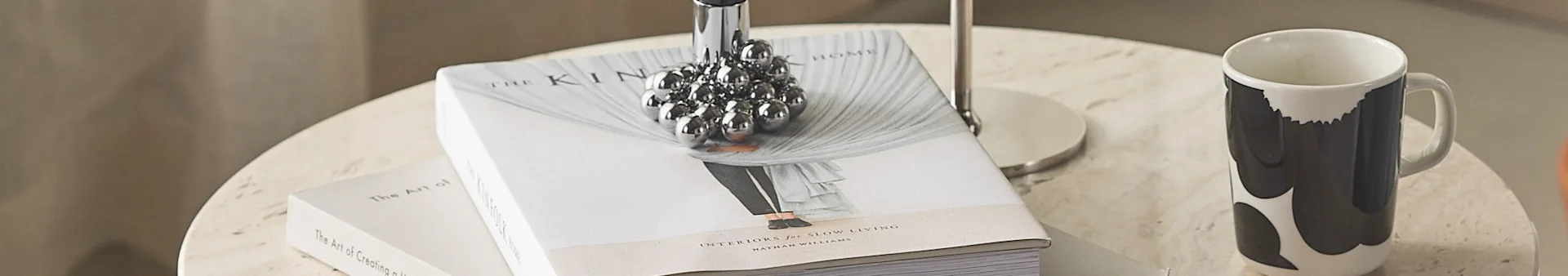 Two books, a silver spiky decorative object, and a white mug with black patterns on a light stone table.