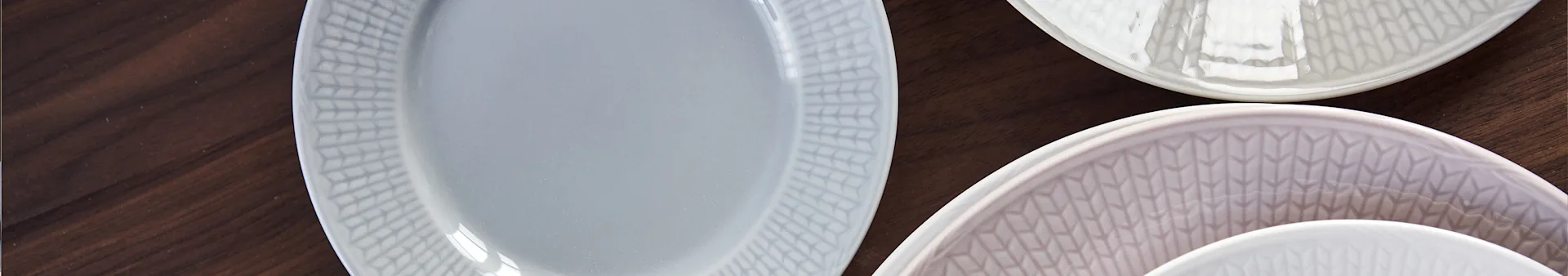 Three patterned ceramic plates in grey, brown, and white on a dark wooden surface.