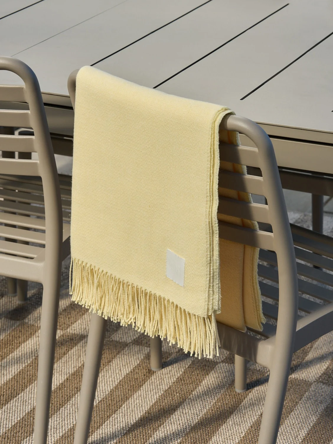 Light yellow blanket with fringes draped over a beige outdoor chair.
