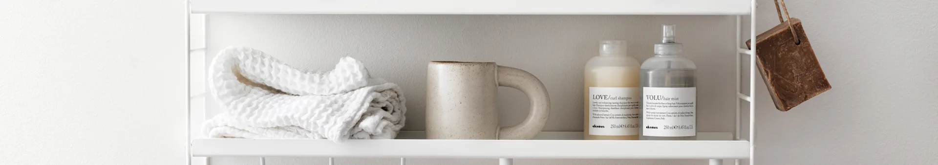 White waffle towel, speckled mug, and two cosmetic bottles on a white shelf. A bar of brown soap hangs to the right.