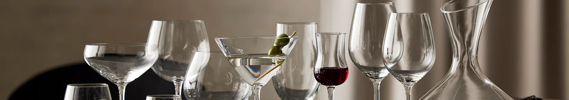 Collection of elegant clear glassware: various wine glasses, a martini glass with olives, and a decanter.